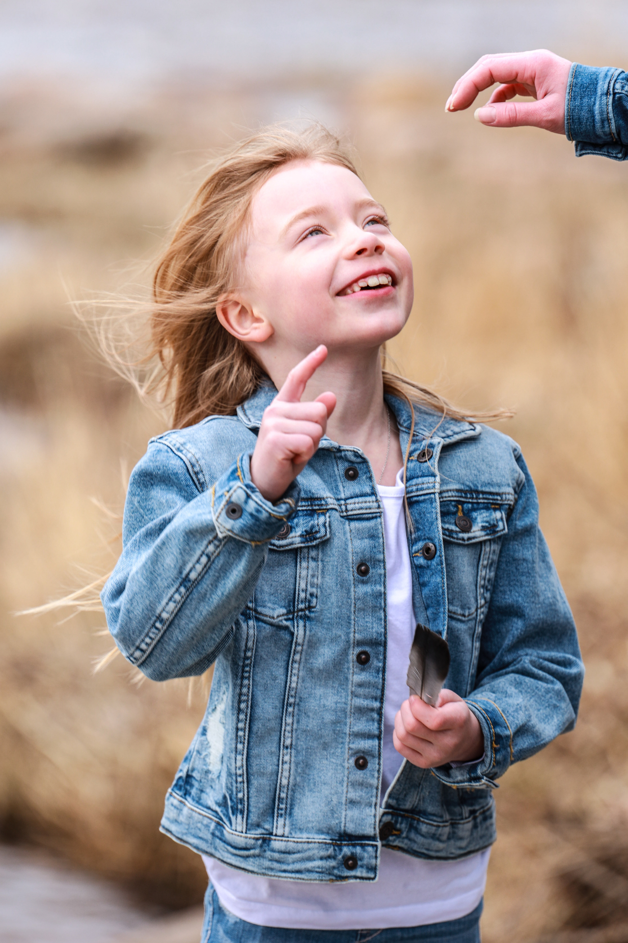 Smiling girl in denim jacket reaching for a feather