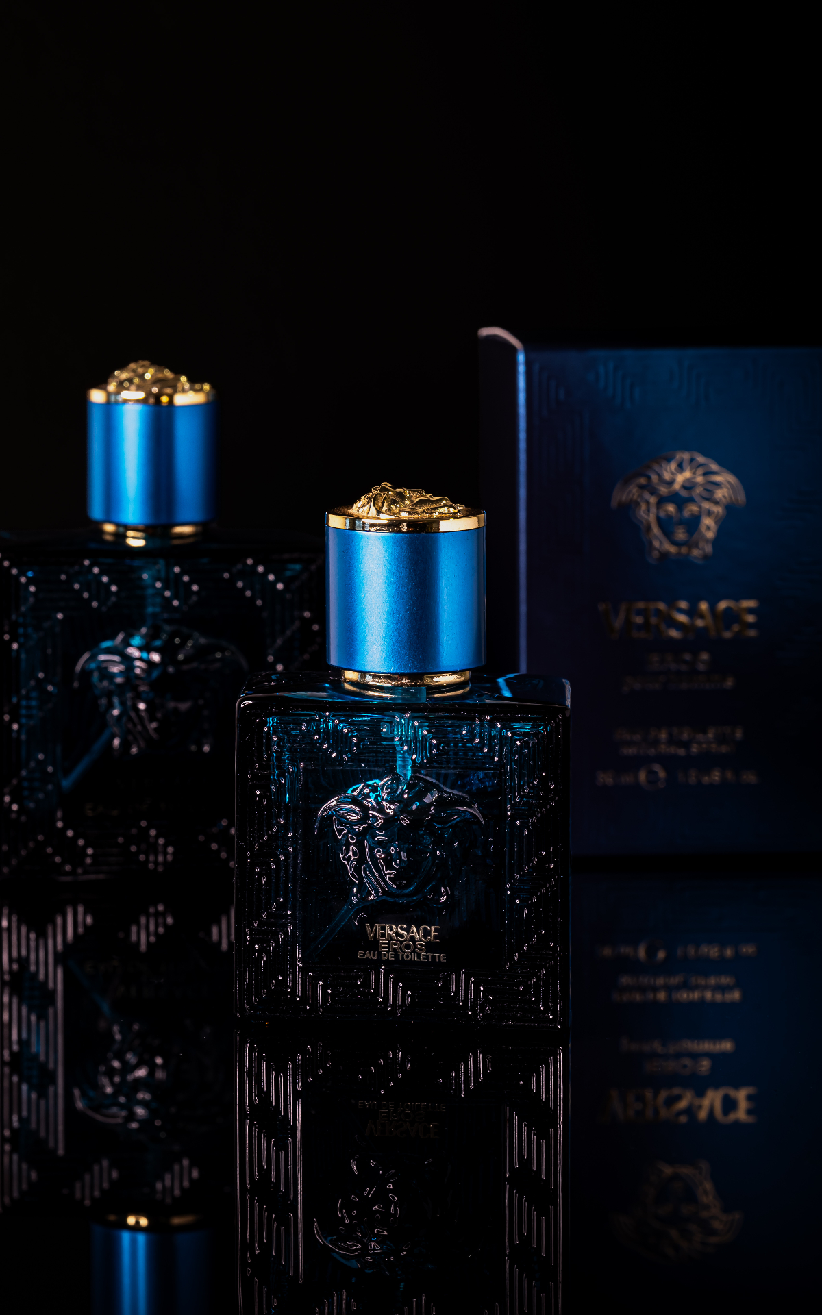 Blue fragrance bottle with gold cap on a dark reflective surface